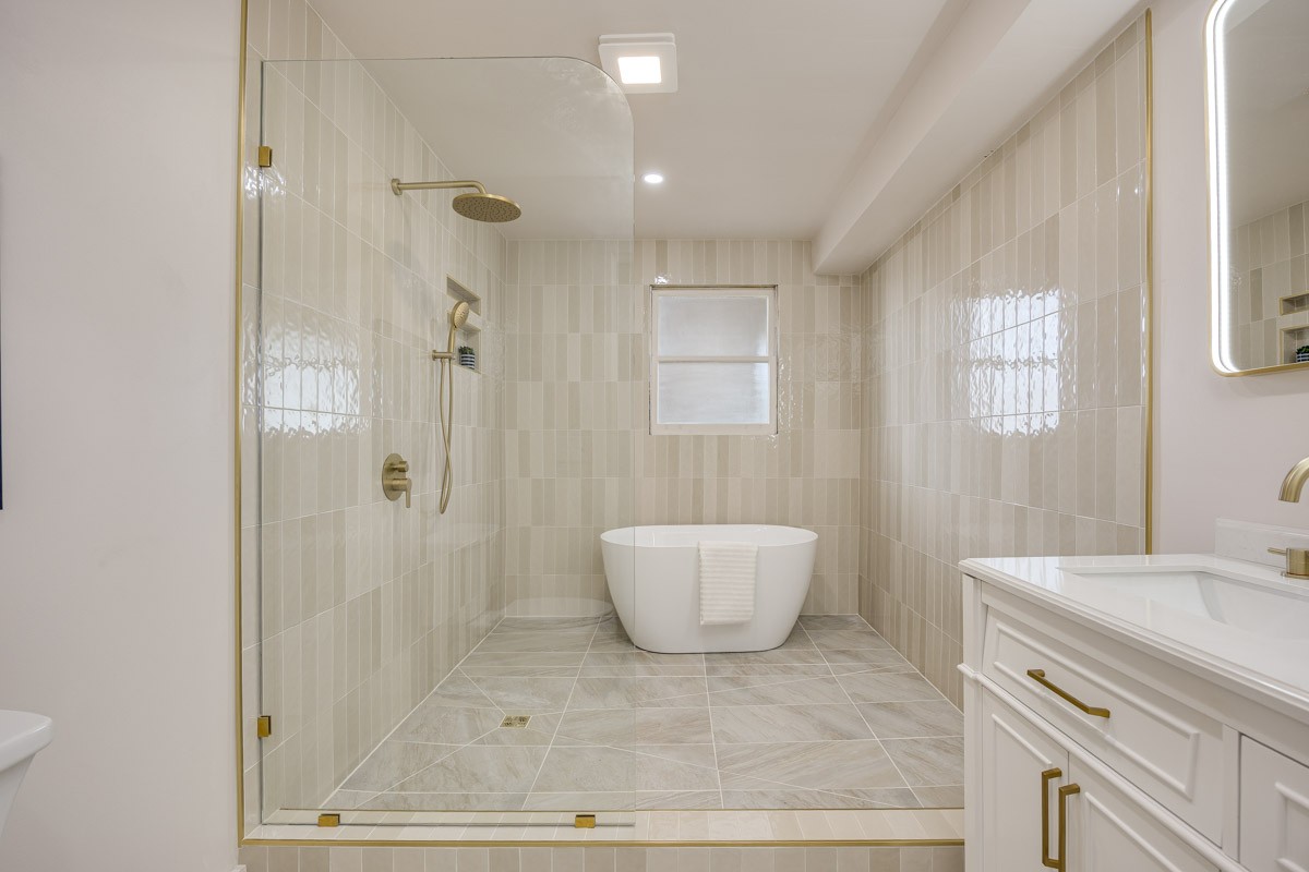 Bathroom with a glass walk-in shower, freestanding tub, and white vanity with brass hardware.