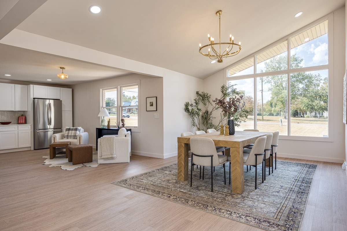 Open dining and living area with tall vaulted windows, a wood table, and an adjoining kitchen.