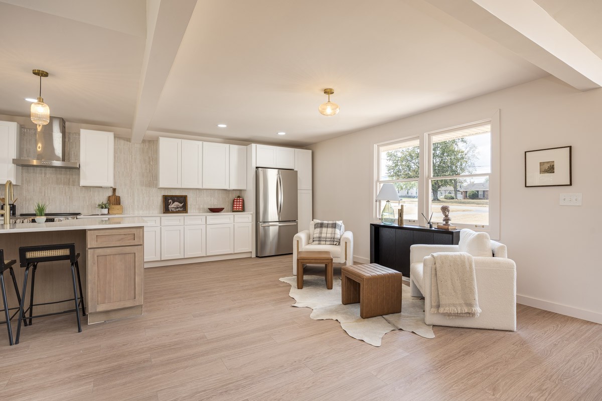 Open-plan kitchen and living area with white cabinetry, stainless-steel appliances, and a window-side seating area.
