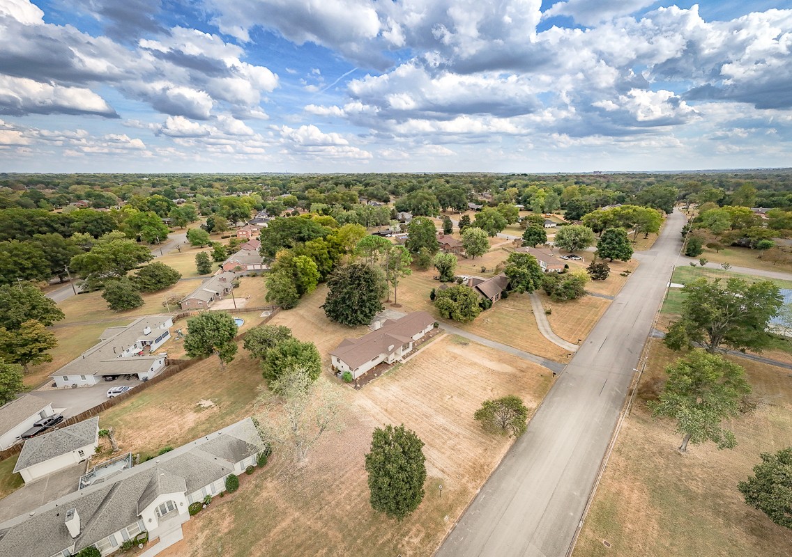 Aerial view of a home and surrounding neighborhood along a paved residential road.