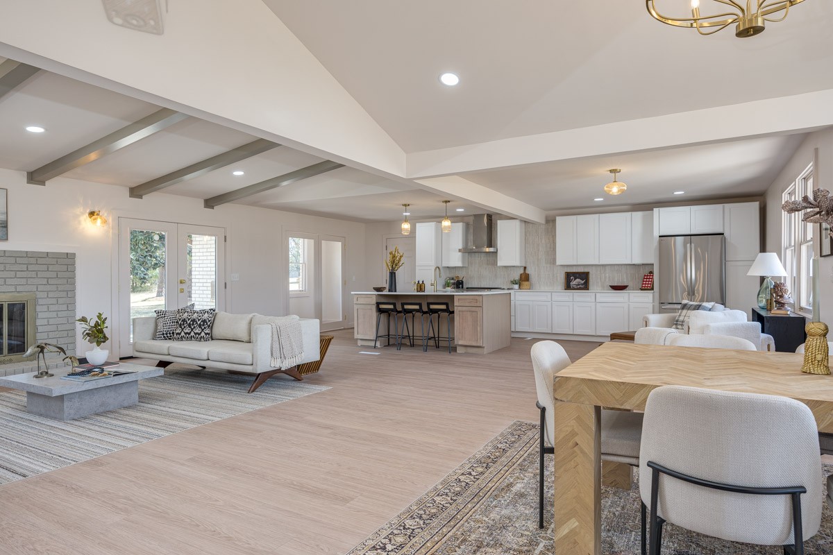 Open-plan living room, dining area, and kitchen with exposed beams and white cabinetry.