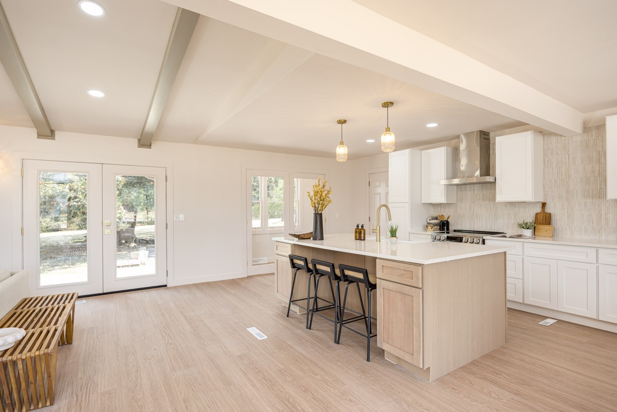 Bright kitchen with a light-wood island, three stools, white cabinets, and glass doors to the yard.