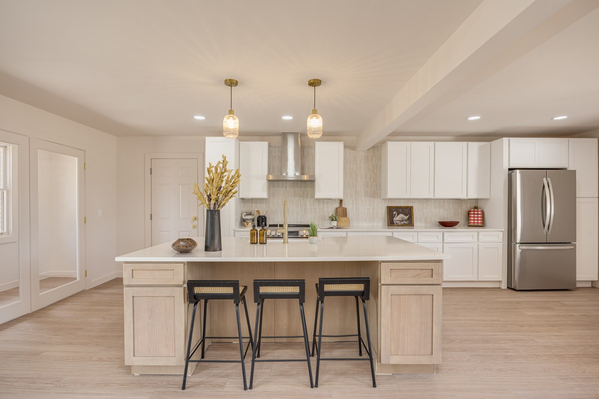 Renovated kitchen with a large light-wood island, white cabinets, and three black bar stools.