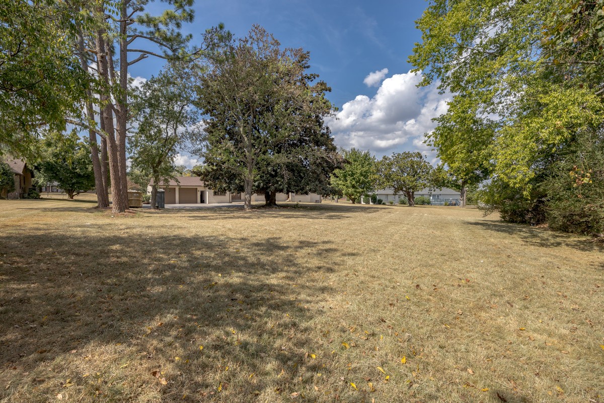 Broad grassy yard with mature shade trees and neighboring homes beyond.