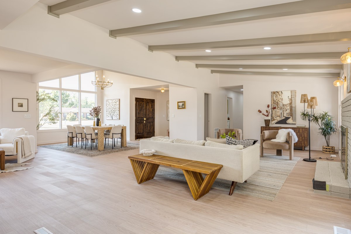 Open-plan living and dining room with exposed beams, large windows, and a fireplace.
