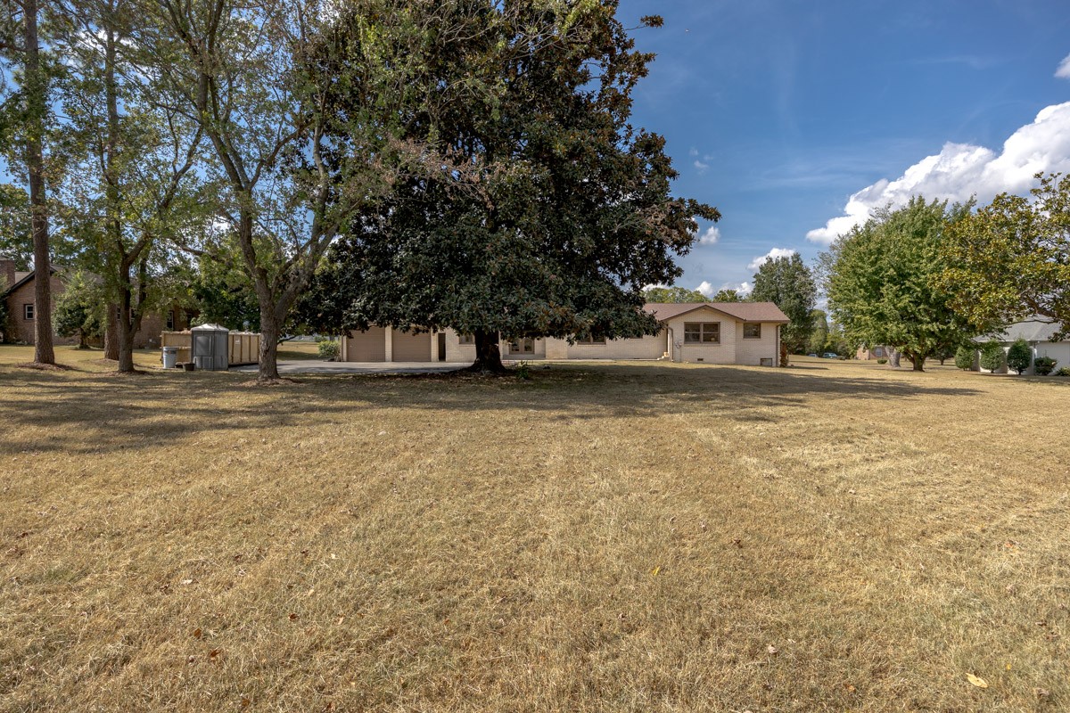 Single-story brick home behind a large magnolia tree, with a broad dry lawn.