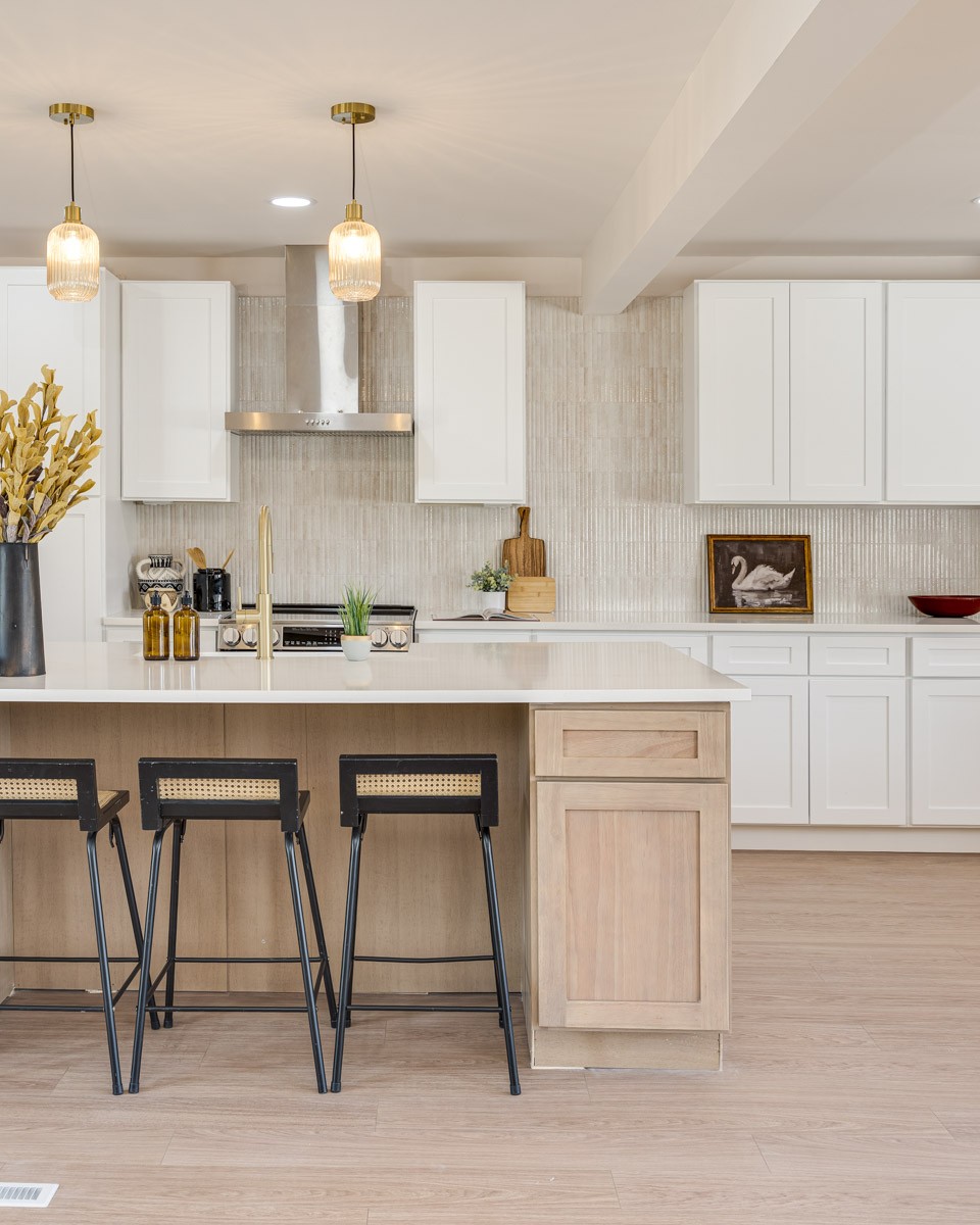 Kitchen with a light wood island, white cabinets, brass pendants, and black stools.