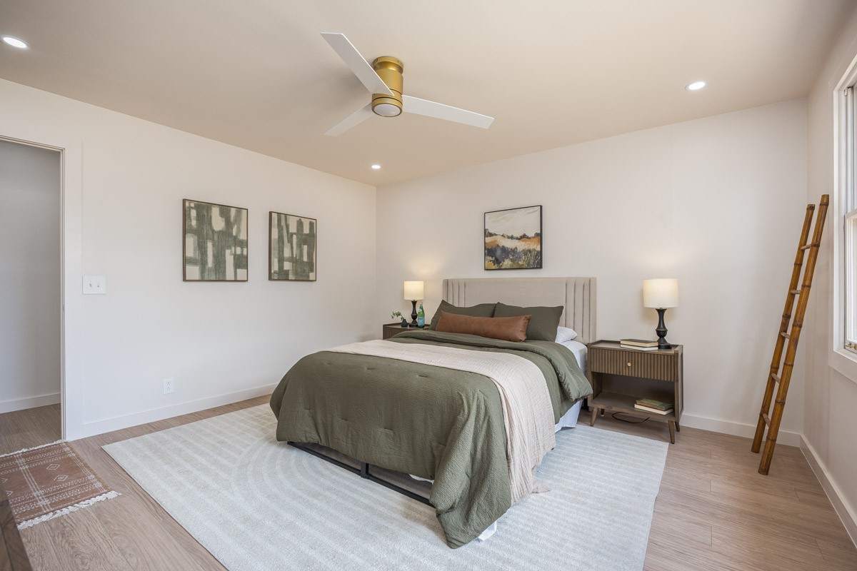 Staged bedroom with olive green bedding, upholstered headboard, and matching bedside tables.