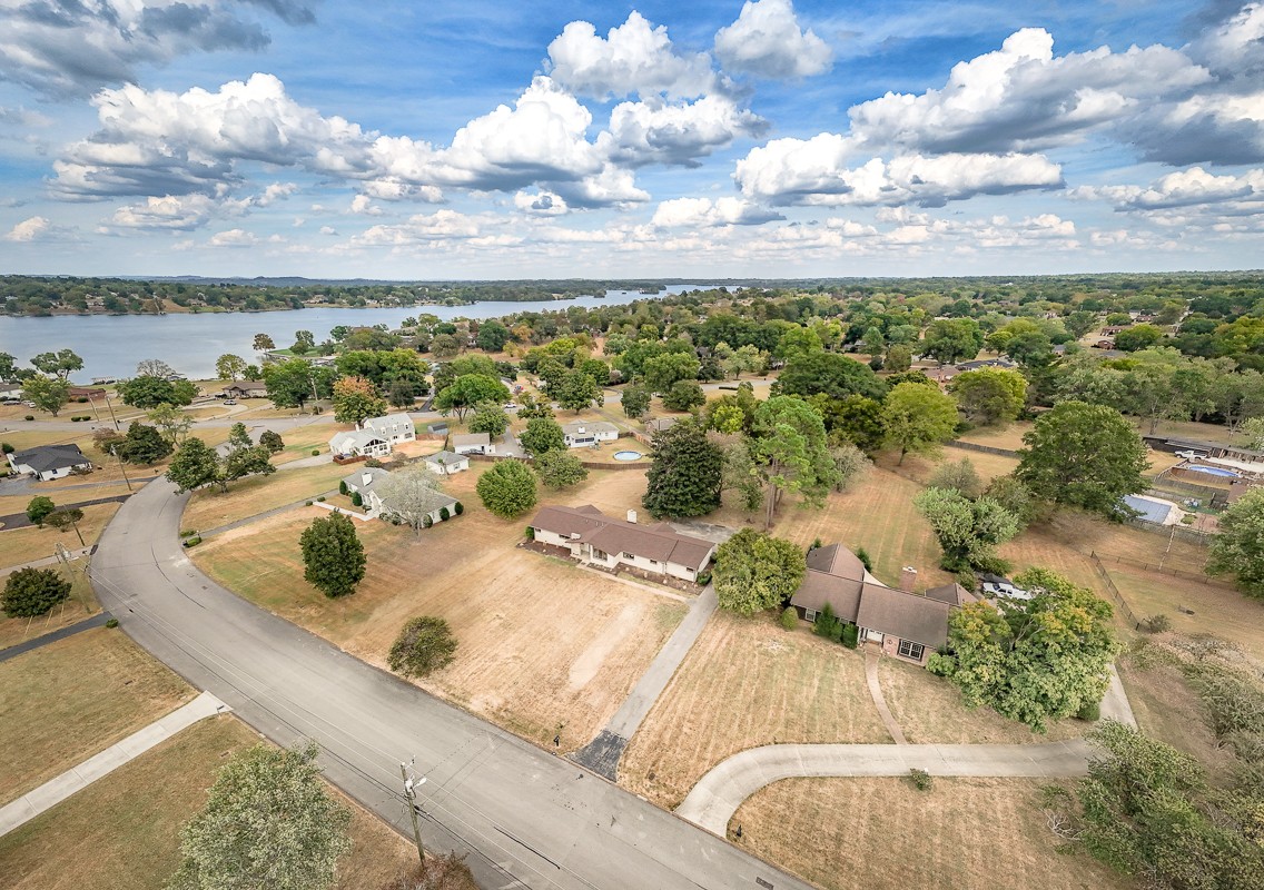 Aerial view of homes along a curving road, with a lake and wooded shoreline beyond.