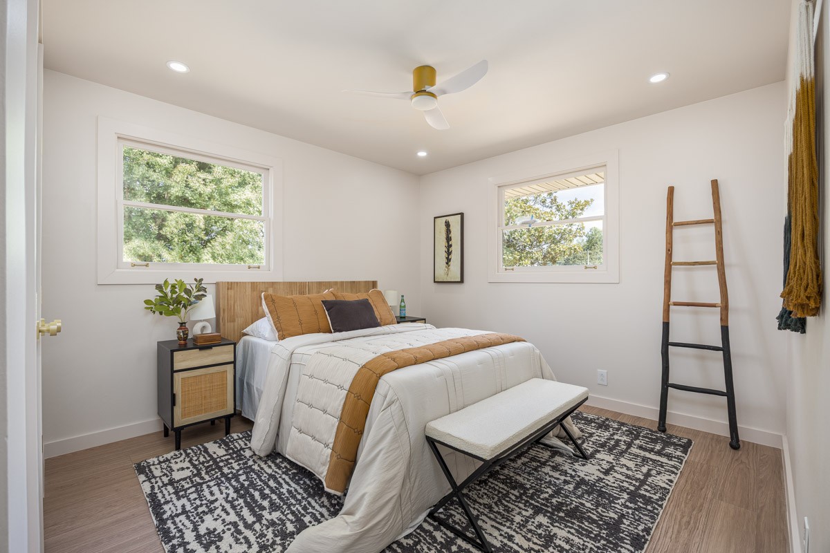 Furnished bedroom with a white bed, wood headboard, two windows, and a patterned rug.
