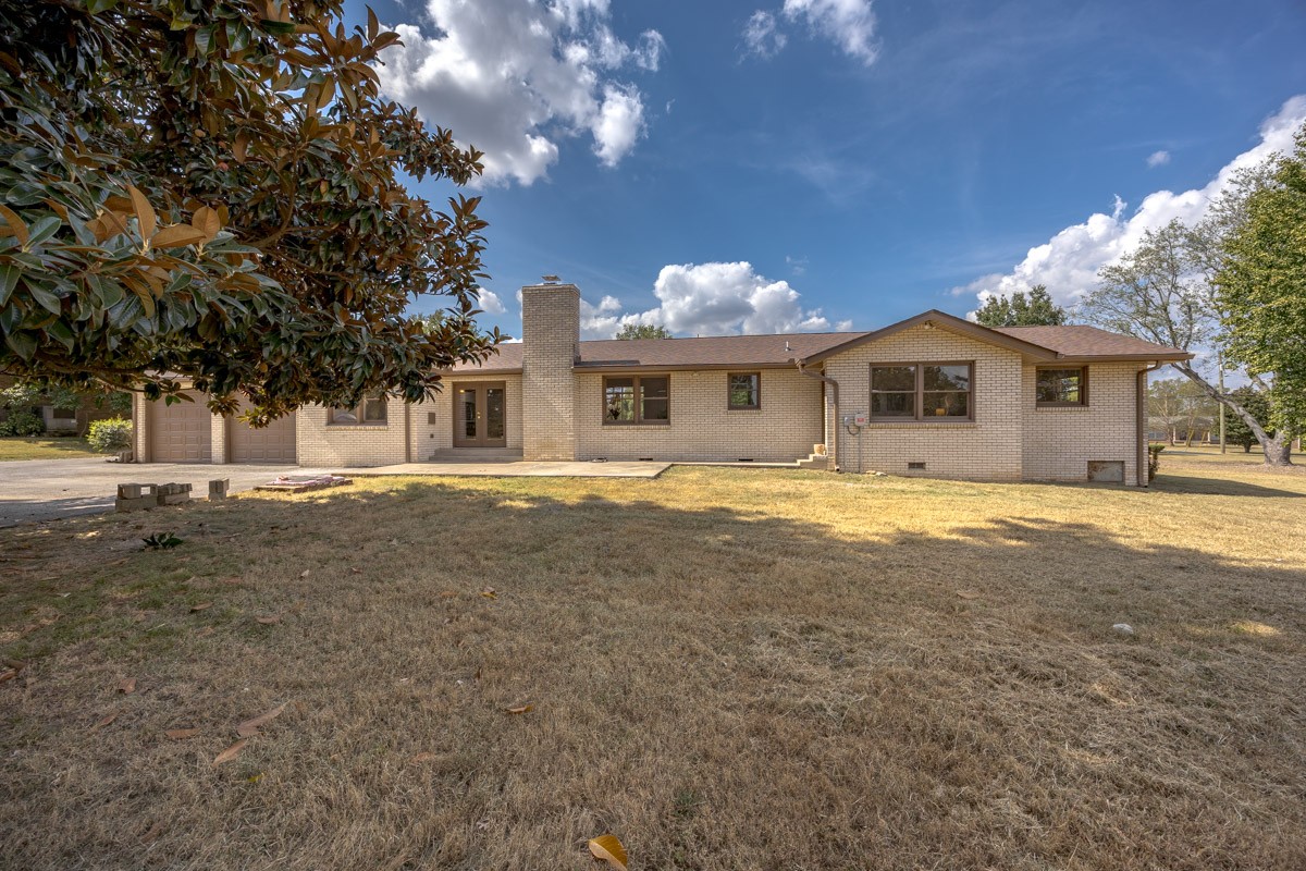 Single-story brick home with an attached garage, broad lawn, and large tree framing the exterior.