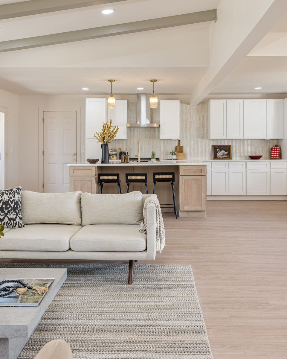 Open-plan kitchen and living room with a wood island, white cabinets, and a cream sofa.