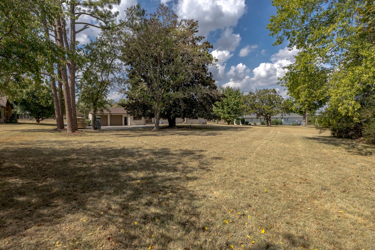 Spacious lawn with mature trees and a low residential building in the background.
