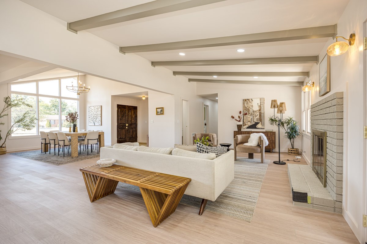 Open-plan living and dining room with exposed beams and a white brick fireplace.