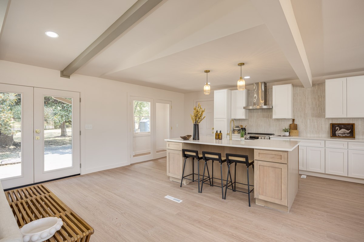 Open-plan kitchen with a large wood island, black stools, white cabinets, and glass doors to the yard.