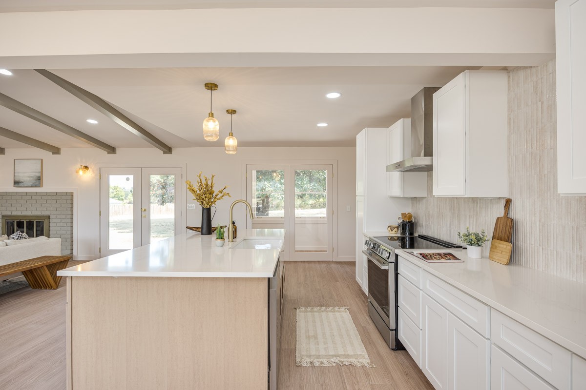 Bright kitchen with a large island, white cabinetry, and an adjoining living area with a brick fireplace.