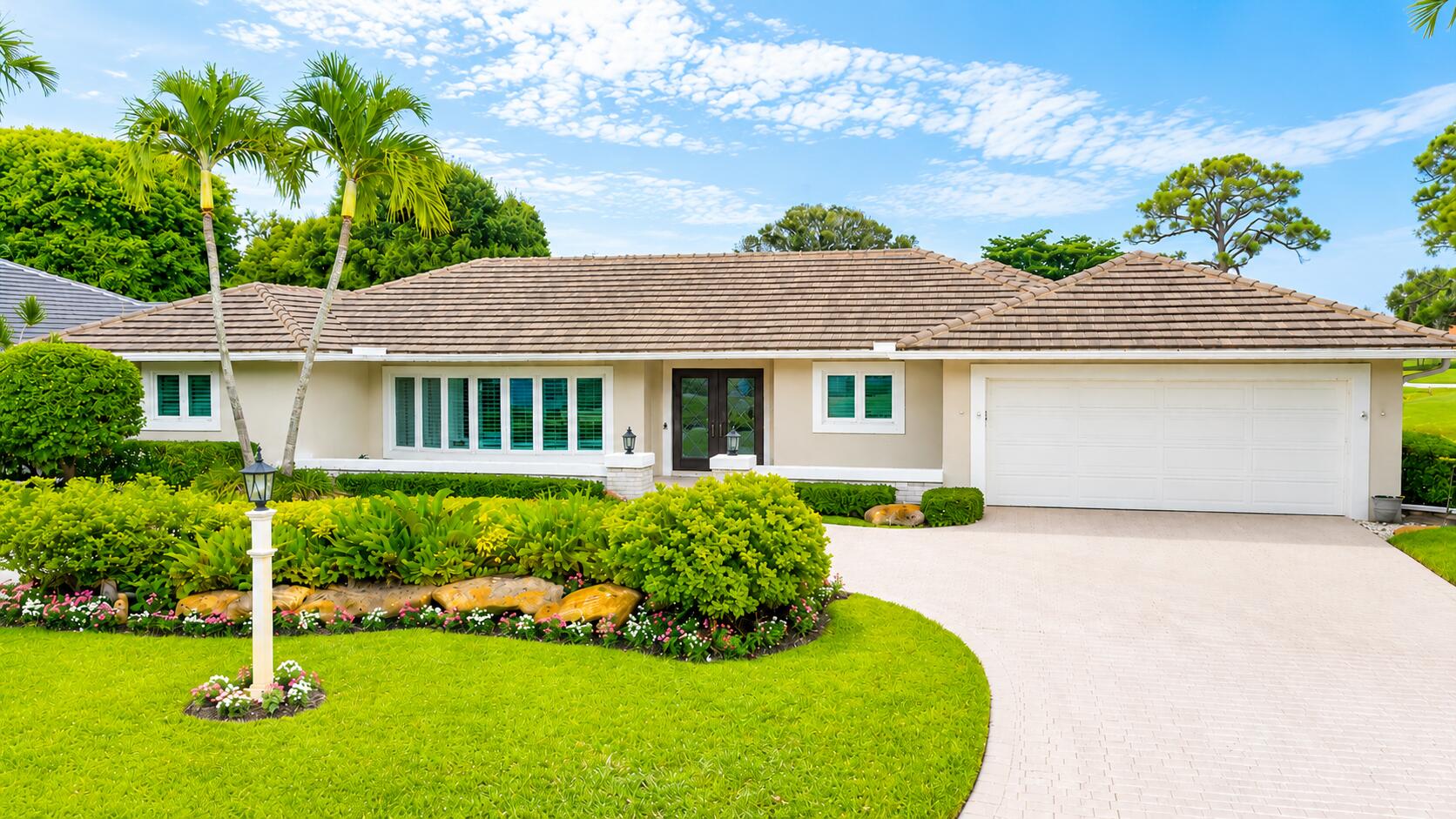 Single-story home with a tiled roof, tropical landscaping, and a curved driveway.