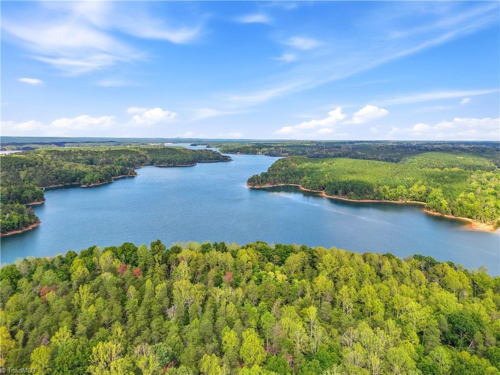 Aerial view of a broad lake winding between forested shorelines beneath a blue sky.