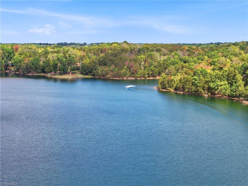 Aerial view of a lake bordered by autumn-colored woods, with a boat wake on the water.