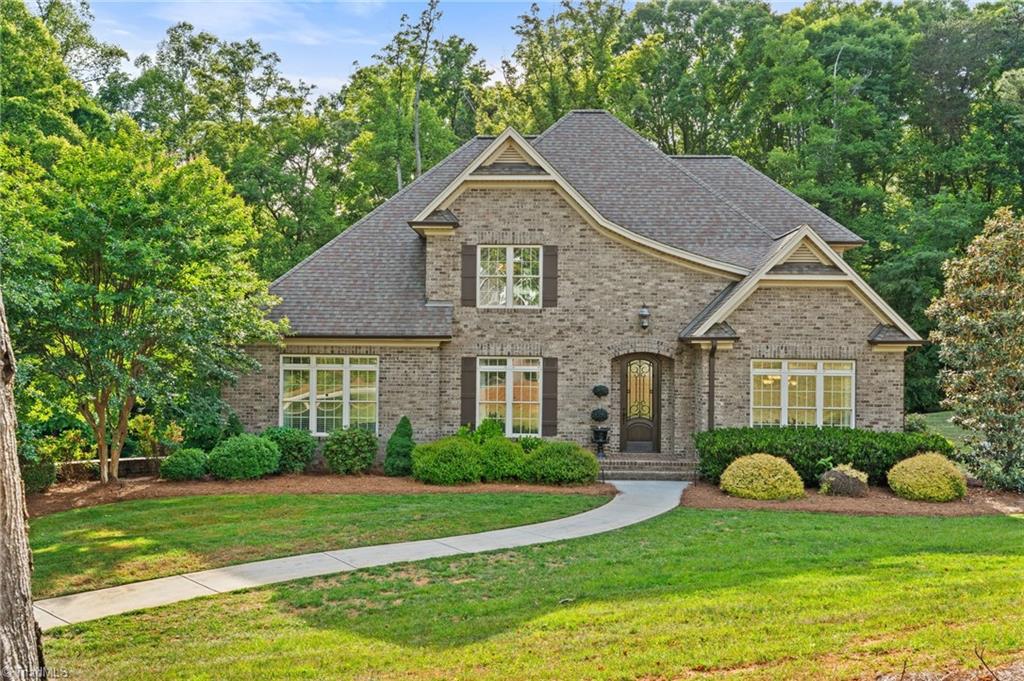 Two-story brick home with a gabled roof, landscaped lawn, and curved walkway to the front door.