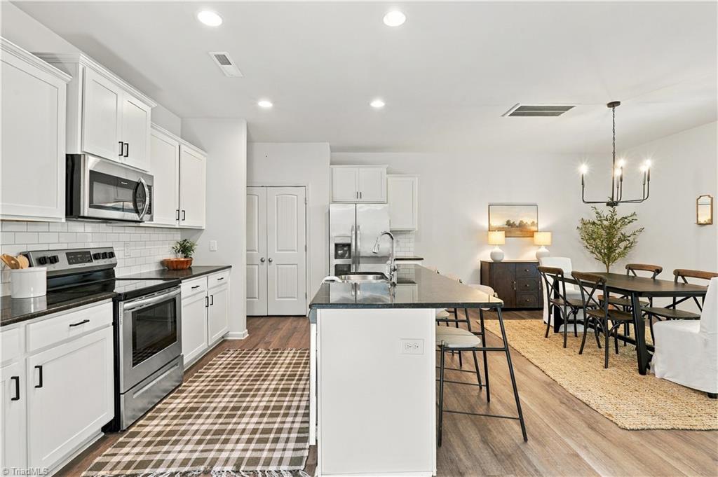 Open-plan kitchen and dining area with white cabinets, stainless steel appliances, and a central island.
