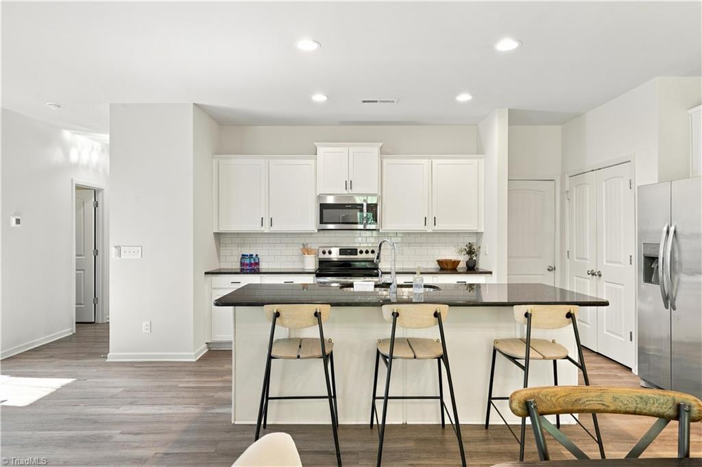 Kitchen with a large island, three bar stools, white cabinets, and stainless steel appliances.