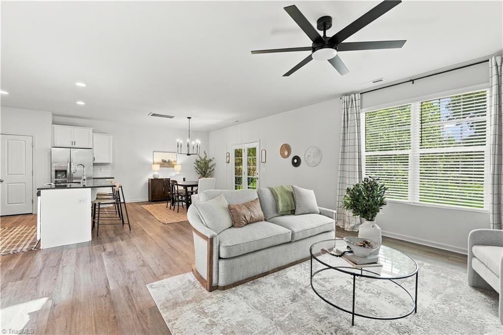 Open-plan living room with gray sofa, large windows, and kitchen and dining area beyond.