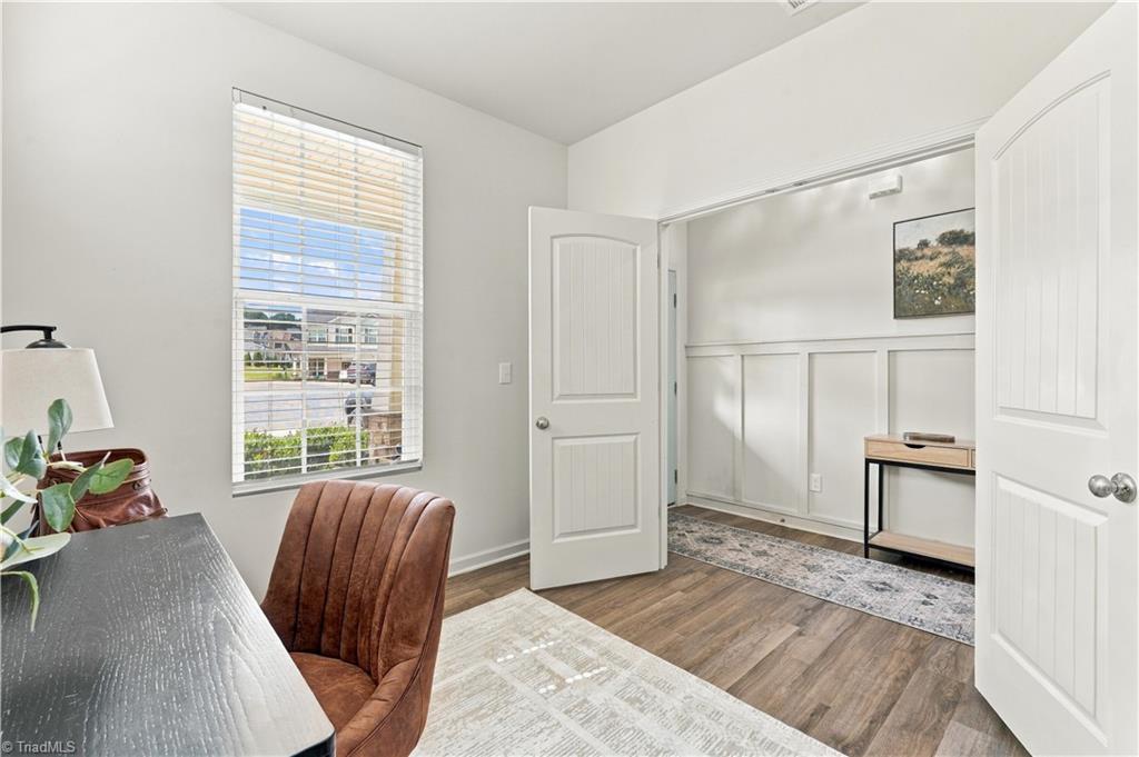 Furnished home office with a brown chair, dark desk, and open doors to a wainscoted room.
