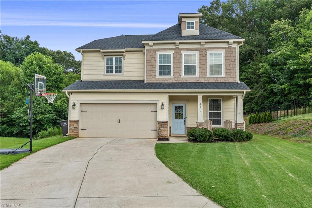 Two-story beige home with a blue front door, double garage, basketball hoop, and broad driveway.