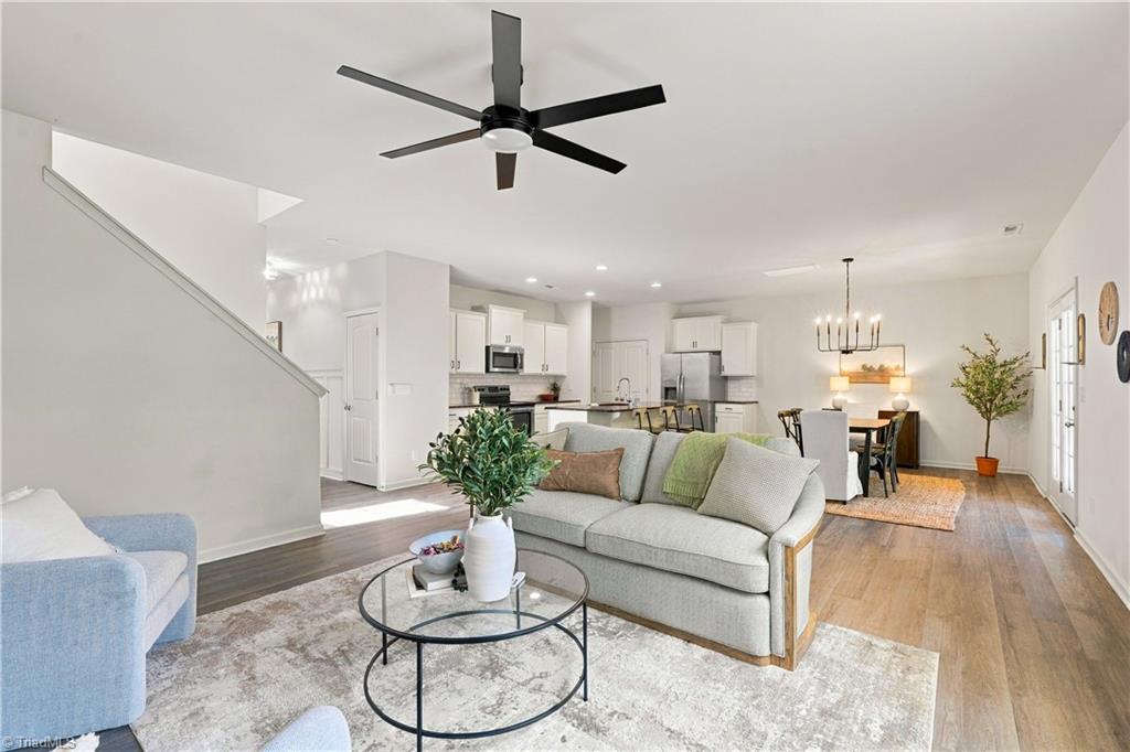 Open-plan living room with gray sectional, glass coffee table, and kitchen and dining area beyond.