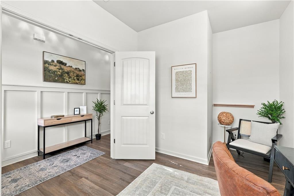 Staged sitting room with paneled walls, a console table, patterned rugs, and a cushioned chair beside an open door.