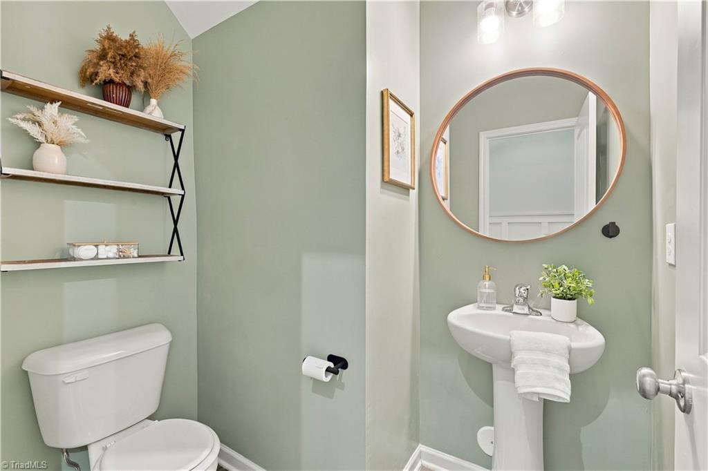 Powder room with sage-green walls, open shelves above the toilet, and a pedestal sink beneath a round mirror.
