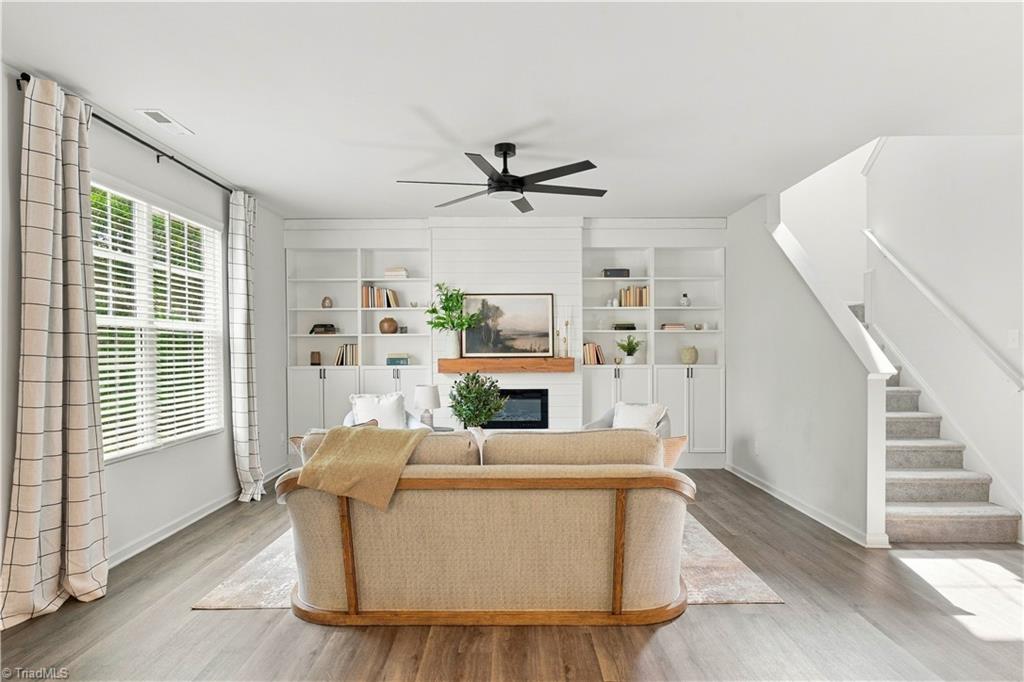 Staged living room with built-in bookcases, fireplace, large windows, and staircase.
