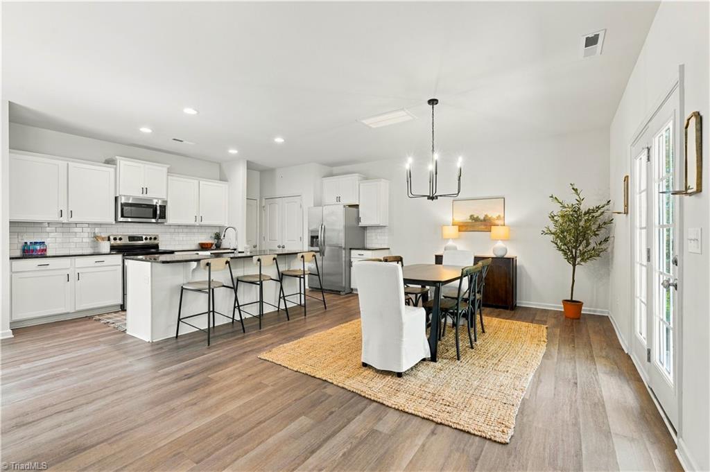 Open-plan kitchen and dining area with a white island, bar stools, and dining table by French doors.