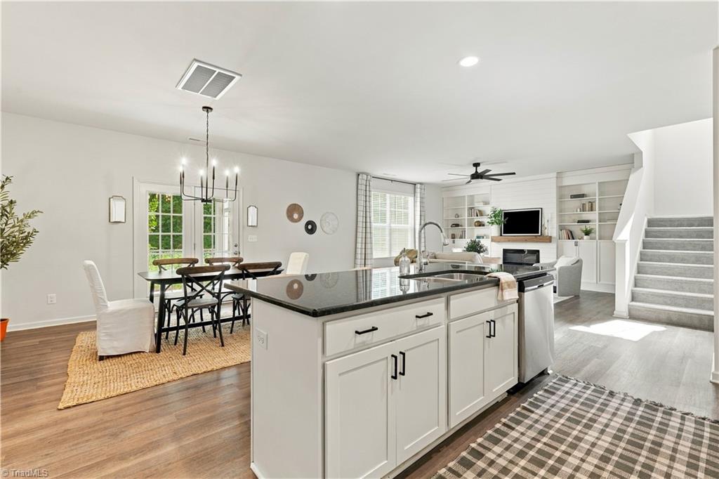 Open kitchen with a large dark-stone island adjoining a dining area and built-in living room shelving.