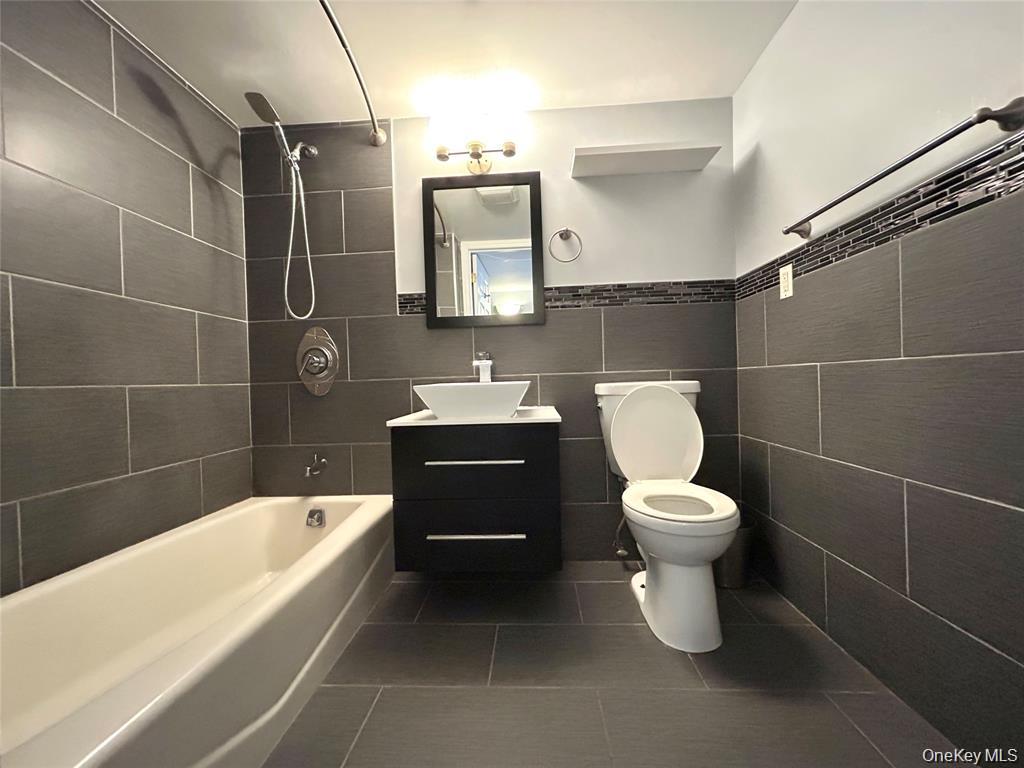 Bathroom with a white bathtub, dark tile, black vanity, vessel sink, and toilet.