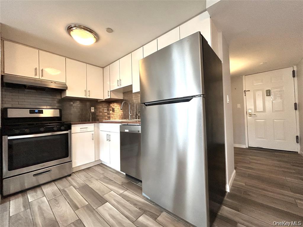 Apartment kitchen with white cabinets, stainless steel appliances, and dark tile backsplash.