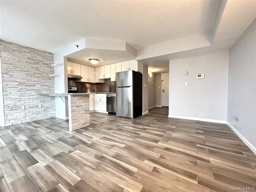Open kitchen and living area with white cabinets, stainless appliances, and gray wood-look tile floors.