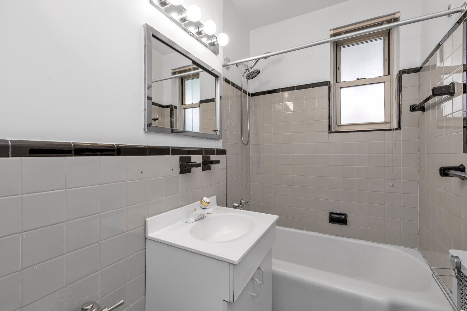 Bathroom with a white vanity, tiled tub and shower, large mirror, and window.