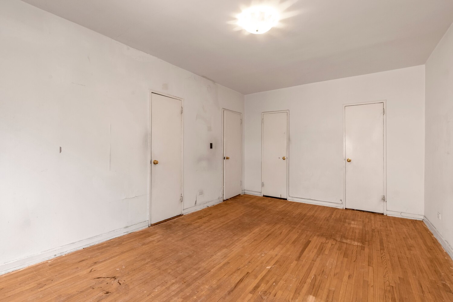 Empty apartment room with hardwood floors and several closed doors.