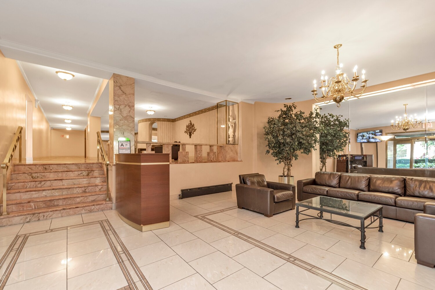 Apartment building lobby with a marble staircase, reception desk, and leather seating.