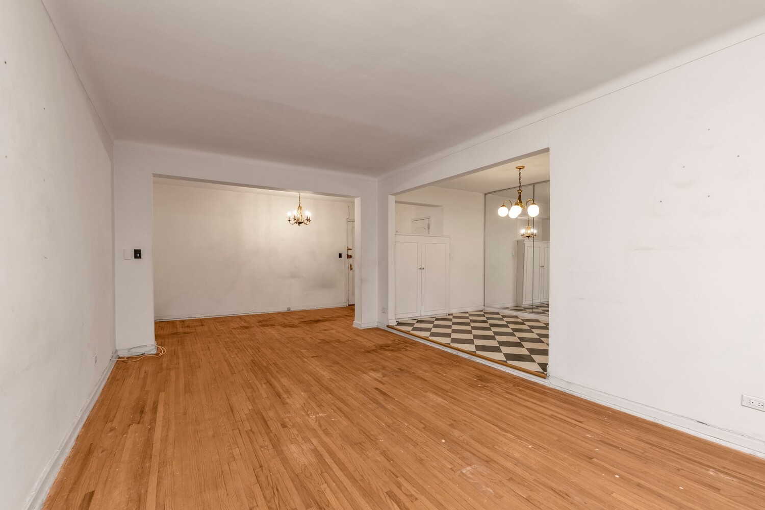 Empty living room with hardwood floors and a view into a checkerboard-tile area.