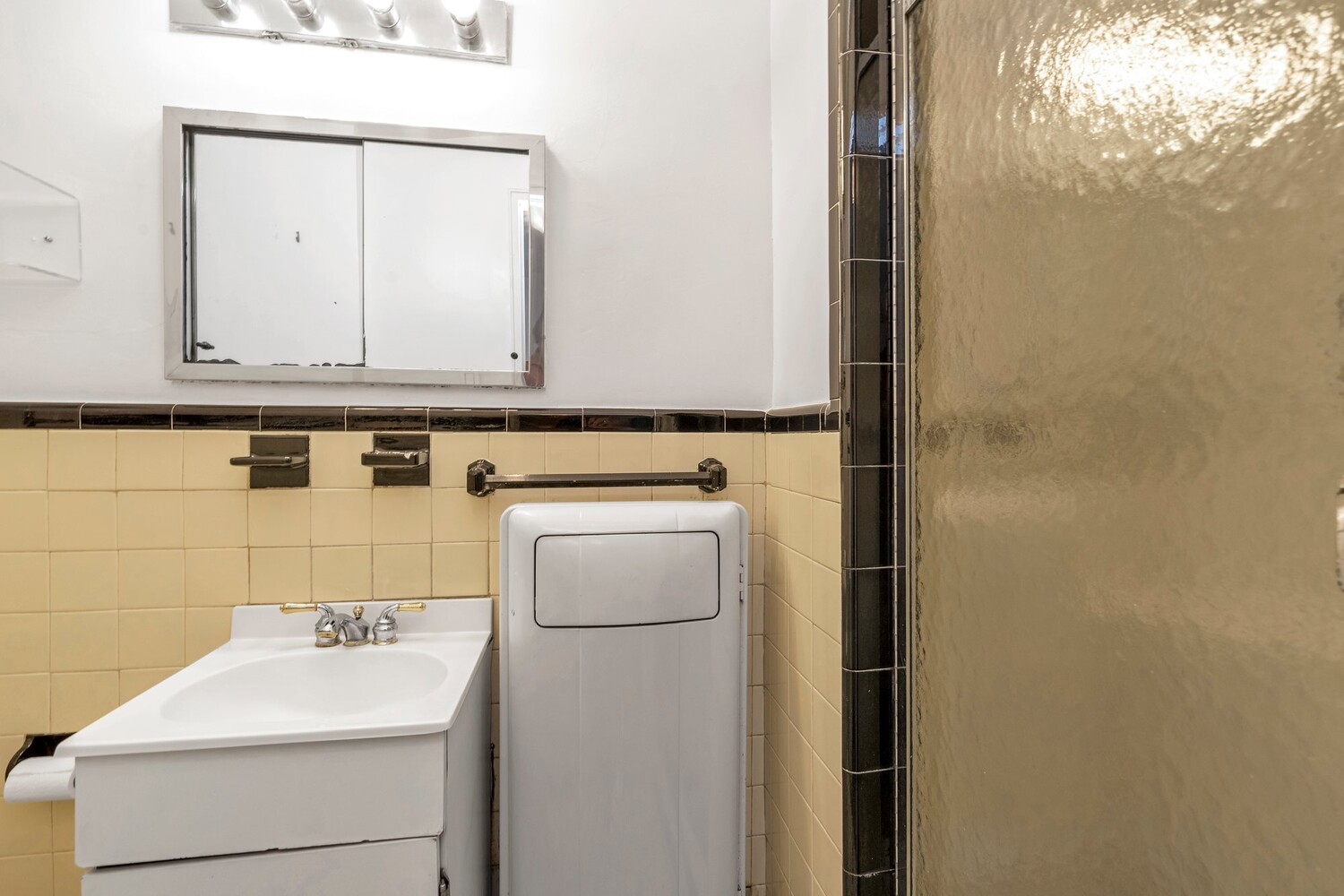 Bathroom with a white vanity, mirrored medicine cabinet, and textured glass shower enclosure.
