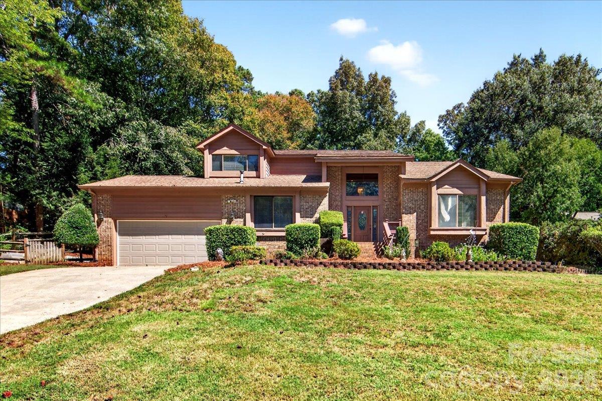 Brick suburban home with a two-car garage, broad lawn, and mature trees.