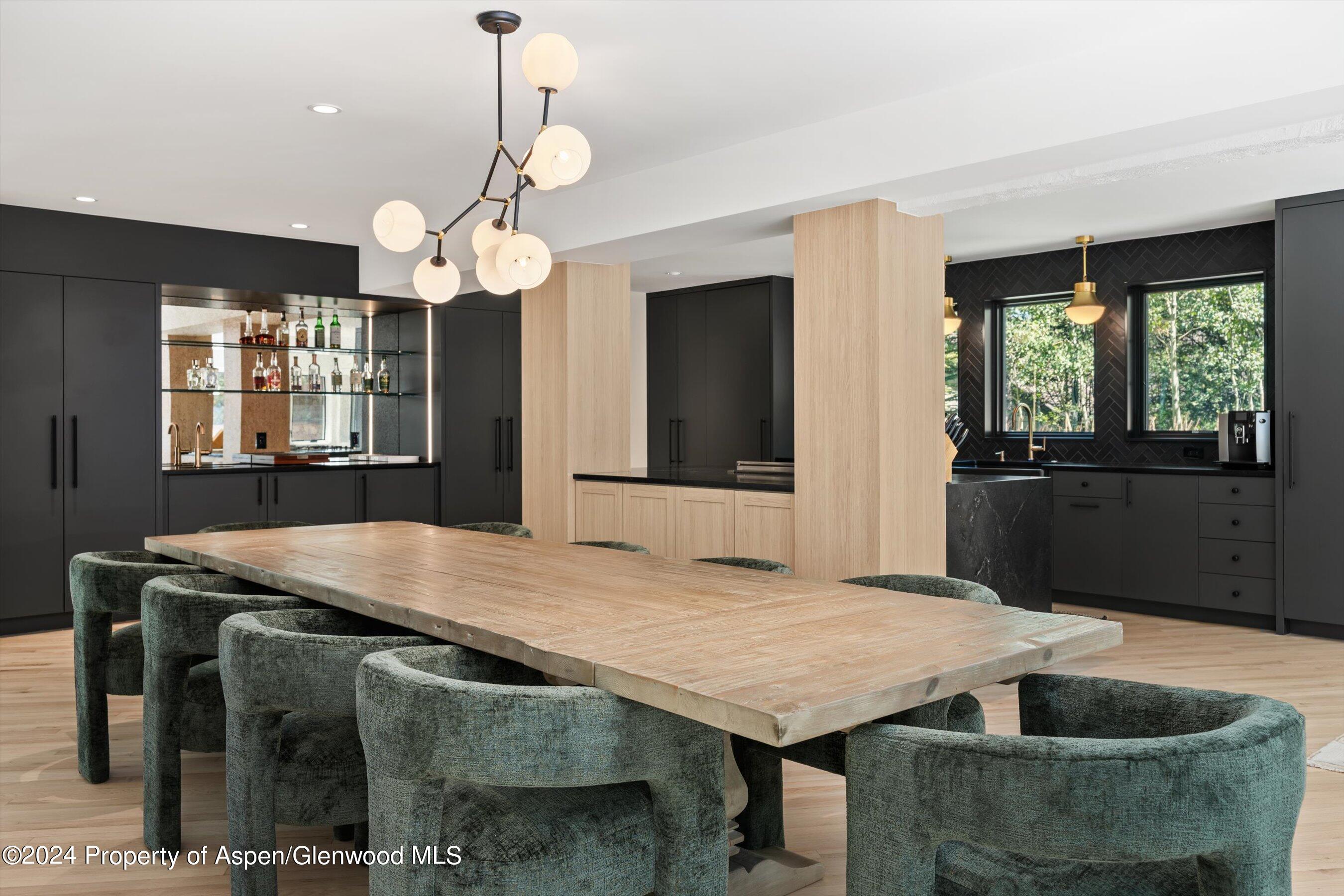 Dining area with a long wood table, upholstered chairs, and a black contemporary kitchen.