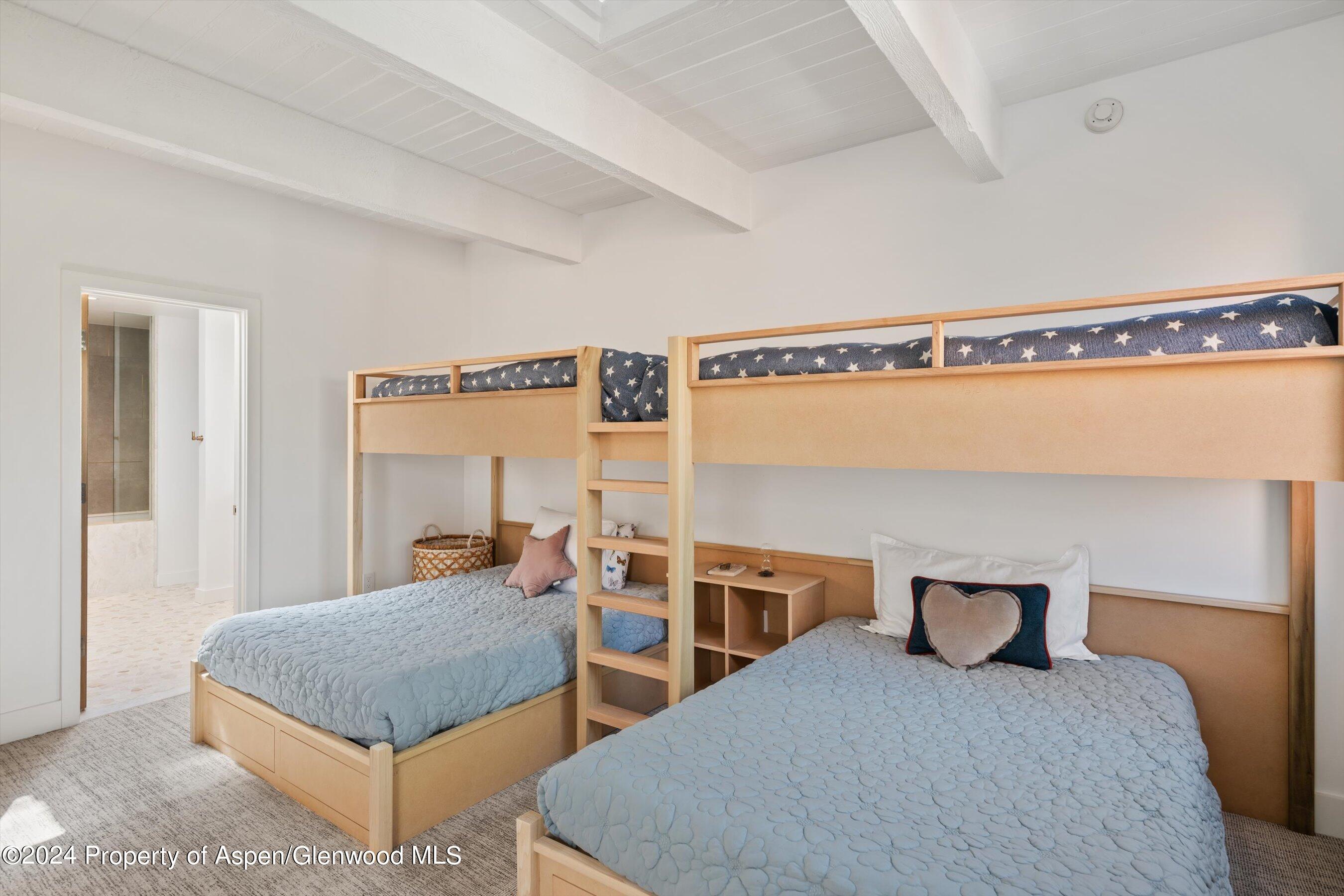 Bedroom with two beds beneath a wooden bunk bed and a doorway to an adjoining bathroom.