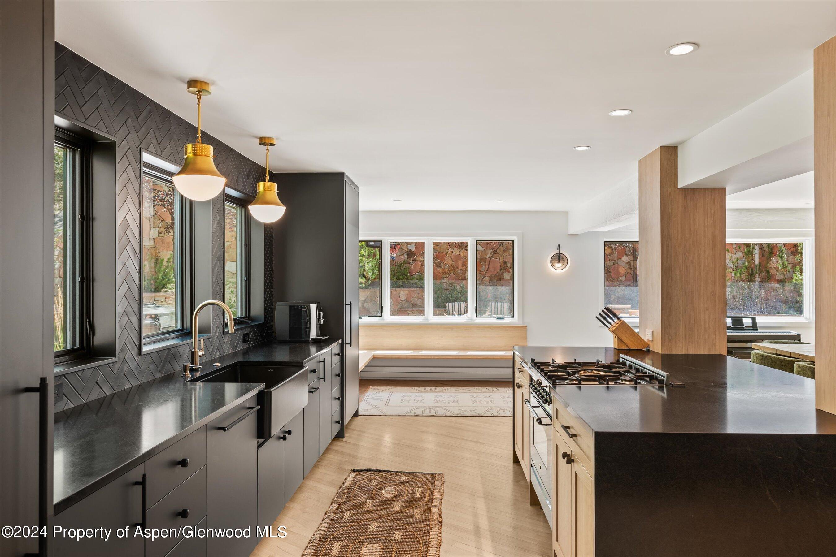Modern kitchen with dark cabinetry, a large gas-range island, and windows overlooking a stone wall.