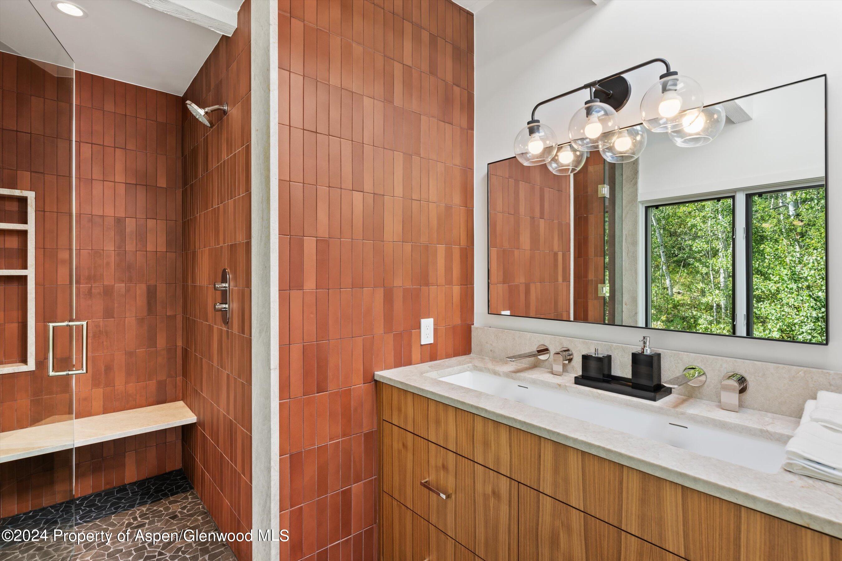 Bathroom with a terracotta-tiled walk-in shower and wood double vanity beneath a wide mirror.