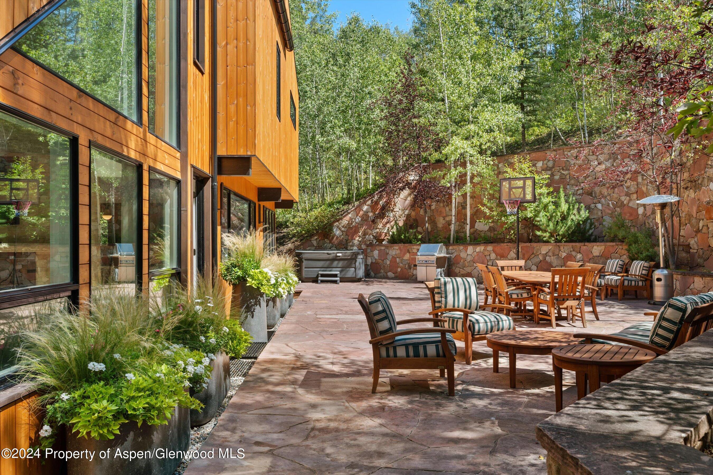 Stone patio with outdoor dining and lounge seating beside a modern wood-sided home.