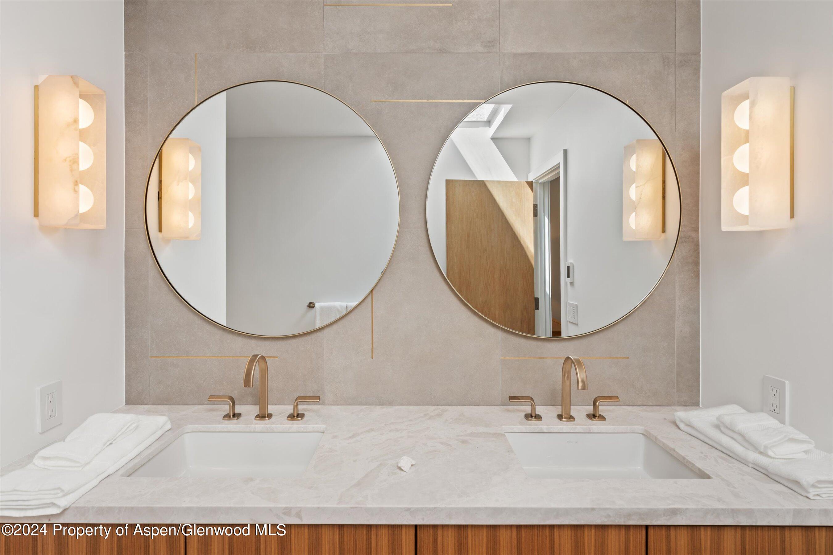 Bathroom vanity with two sinks, round mirrors, brass fixtures, and warm wall sconces.